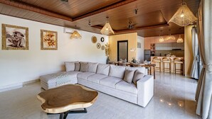 A spacious living area with a large sofa, a wooden coffee table, and a dining area with a kitchen in the background. - The Lotus Villa Uluwatu (Ungasan)