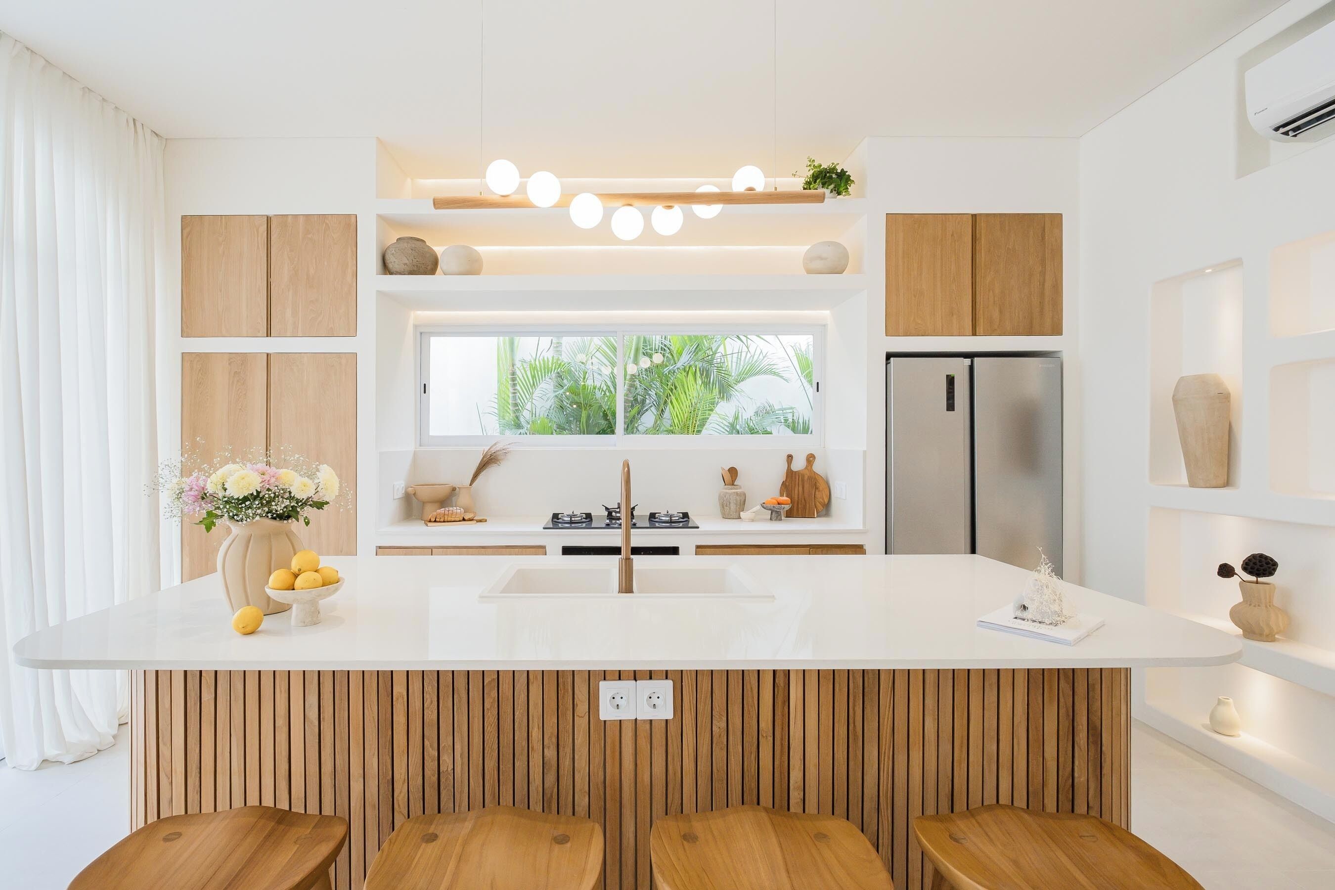 Una cocina moderna con una isla central, armarios de madera, un refrigerador de acero inoxidable y una ventana con vistas al verdor.