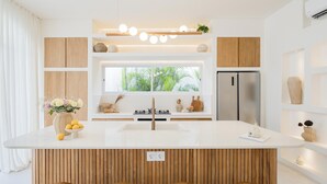 Een moderne keuken met een centraal eiland, houten kasten, een roestvrijstalen koelkast en een raam met uitzicht op groen.