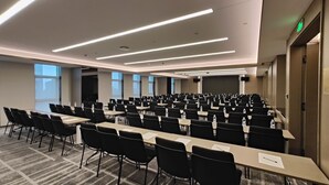 Ett konferensrum med rader av bord och stolar, utrustat med vattenflaskor och en stor skärm längst fram.