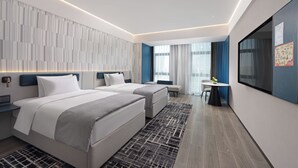Ett modernt hotellrum med två sängar, ett skrivbord och ett stort fönster.