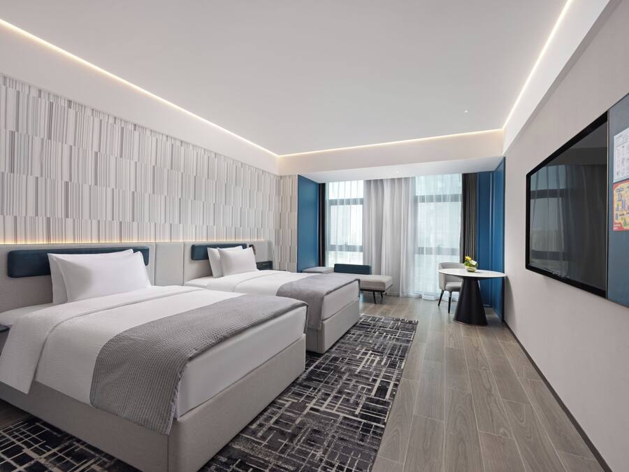 A modern hotel room with two beds, a desk, and a large window.