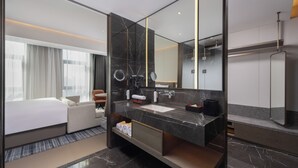 Ett modernt hotellrum med en stor säng, ett badrum med en marmorbeklädd tvättställ och en stor spegel.