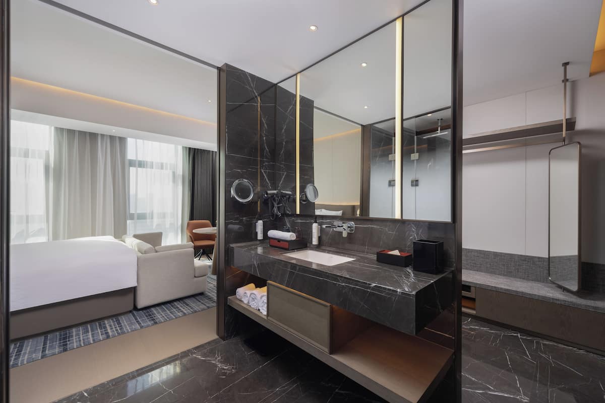 A modern hotel room with a large bed, a bathroom with a marble vanity, and a large mirror.
