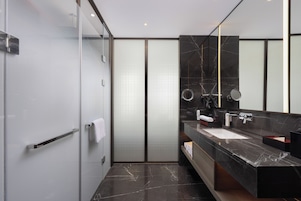 A modern bathroom with a glass shower enclosure, a marble-topped sink, and a large mirror.