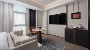 Ett modernt hotellrum med en soffa, ett litet runt bord med en vas, en tv som är monterad på väggen och en minibar.