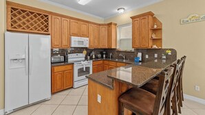 A kitchen with wooden cabinets, a white refrigerator, a microwave, a stove, and a granite countertop. - Vitamin Sea | Easy Beach Living • Community Pool • 3 Min Walk to Beach (South Padre Island)