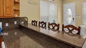 A kitchen with granite countertops, wooden cabinets, and a white door with a glass window. - Vitamin Sea | Easy Beach Living • Community Pool • 3 Min Walk to Beach (South Padre Island)