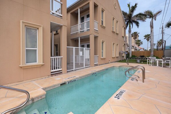 A residential building with a swimming pool, balconies, and palm trees.