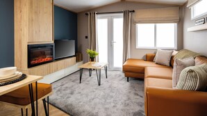 A modern living room with a built-in fireplace, a flat-screen TV, a sofa, and a dining area with a table and chairs. - Spacious, light and contemporary lodge. (Moffat)