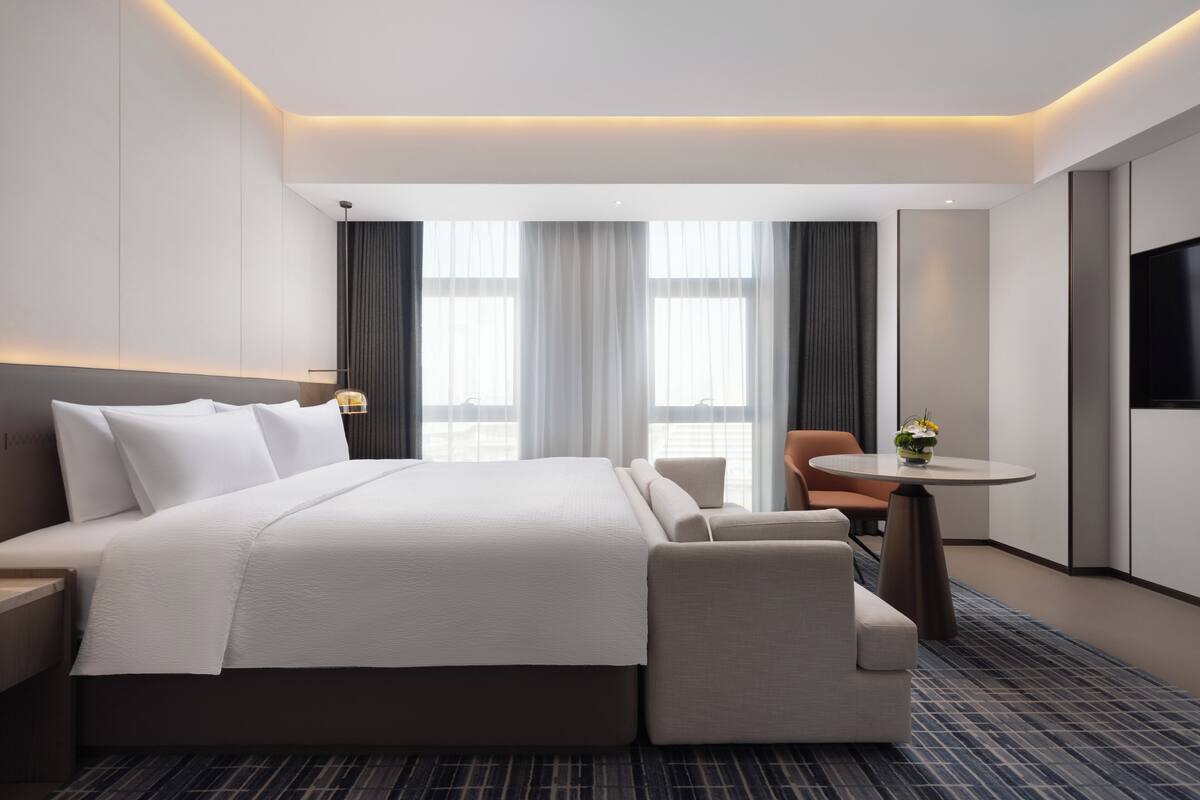 A modern hotel room with a large bed, a seating area, a small table, and a TV.
