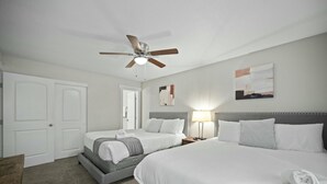 A hotel room with two beds, a ceiling fan, a bedside table with a lamp, and a door. - Spacious and Stylish Apartment | AT&T Stadium (Arlington)
