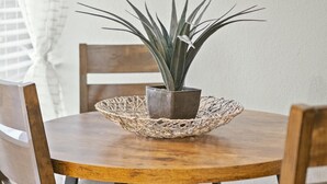 A round wooden dining table with a woven placemat, surrounded by four wooden chairs with grey cushions. A potted plant is placed in the center of the table. - Spacious and Stylish Apartment | AT&T Stadium (Arlington)