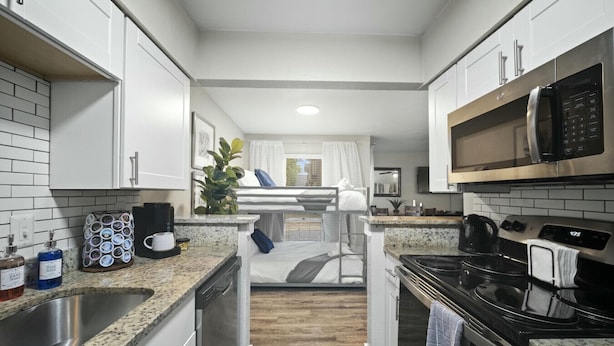 A compact kitchen with white cabinets, a stainless steel sink, a microwave, and a stove. - Spacious and Stylish Apartment | AT&T Stadium (Arlington)