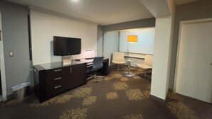 Habitació d'hotel amb televisió de pantalla plana, escriptori amb cadira, làmpada de peu i una catifes amb disseny.