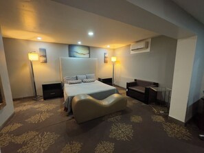A hotel room with a large bed, two bedside lamps, a flat-screen TV, a sofa, and an air conditioning unit. - Hotel Dulce Maria (Tijuana)