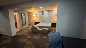 Una habitació d'hotel amb un llit, taules de nit, una cadira, escriptori, mirall i una porta que dona a un bany.
