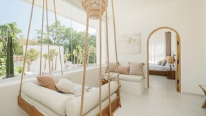 A modern bedroom with a hanging swing, a large window, and a view of greenery. - New 3BR Chic Pool Villa Near Bingin Beach Uluwatu (Bali)