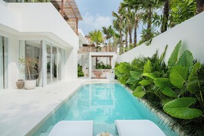 A modern pool area with white lounge chairs, a clear pool, and lush tropical plants. - New 3BR Chic Pool Villa Near Bingin Beach Uluwatu (Bali)