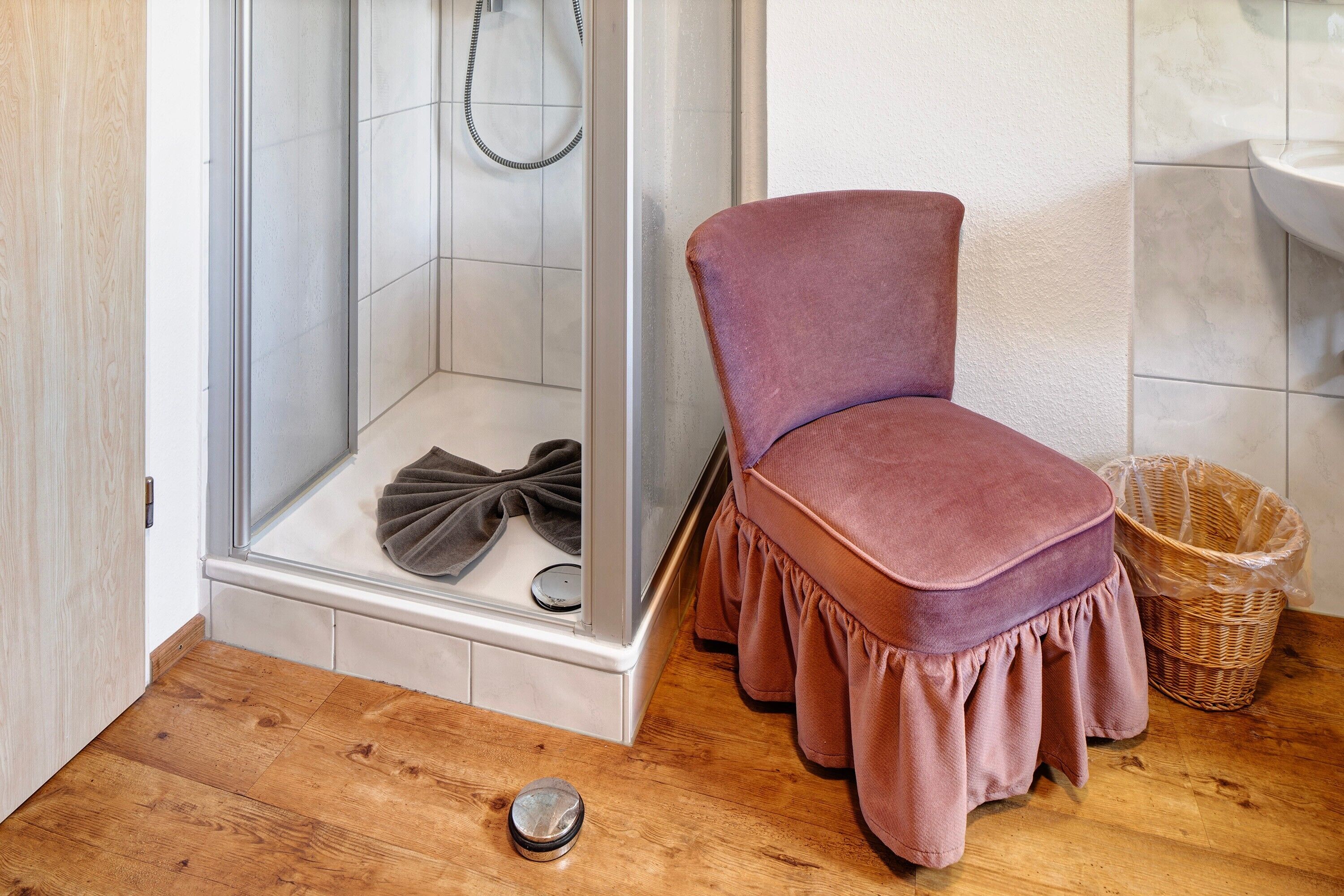 A bathroom with a shower, a chair, a wicker basket, and a wooden floor.