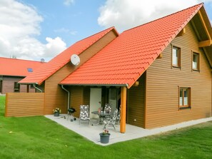 Una casa de madera de dos pisos con techo rojo, un porche cubierto con mobiliario exterior y una antena parabólica.