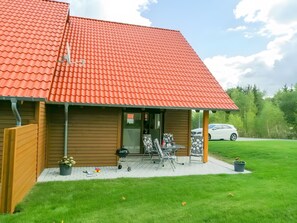 Een gebouw met een rode pannendak, een houten gevel en een overdekte patio met tuinmeubilair.