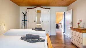 Un dormitorio con dos camas, techo de madera, armario y cómoda.