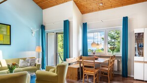 Una habitación moderna con techo de madera, una zona de comedor con mesa y sillas, un sofá, una lámpara y vistas a zonas verdes.