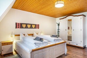Quarto com teto de madeira, cama com roupa de cama branca, guarda-roupa e luminária fixada na parede.