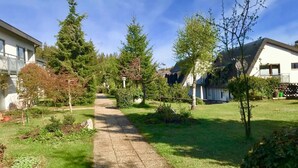 Un sendero atraviesa un jardín con árboles y un edificio a la izquierda.