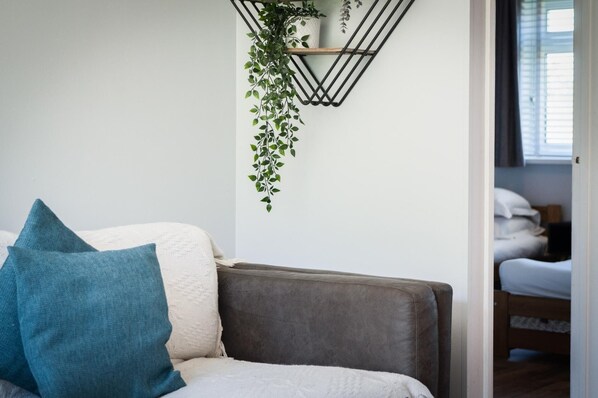 Una sala moderna con un sofá gris, un cojín azul y una planta colgante.