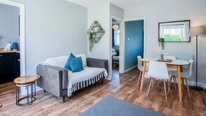 Una sala de estar moderna con un sofá gris, una mesa redonda de madera y un comedor con sillas blancas.