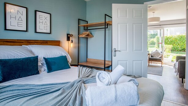 Una cama bien hecha con almohadas, una mesita de noche con lámpara y una puerta que da a un espacio al aire libre.
