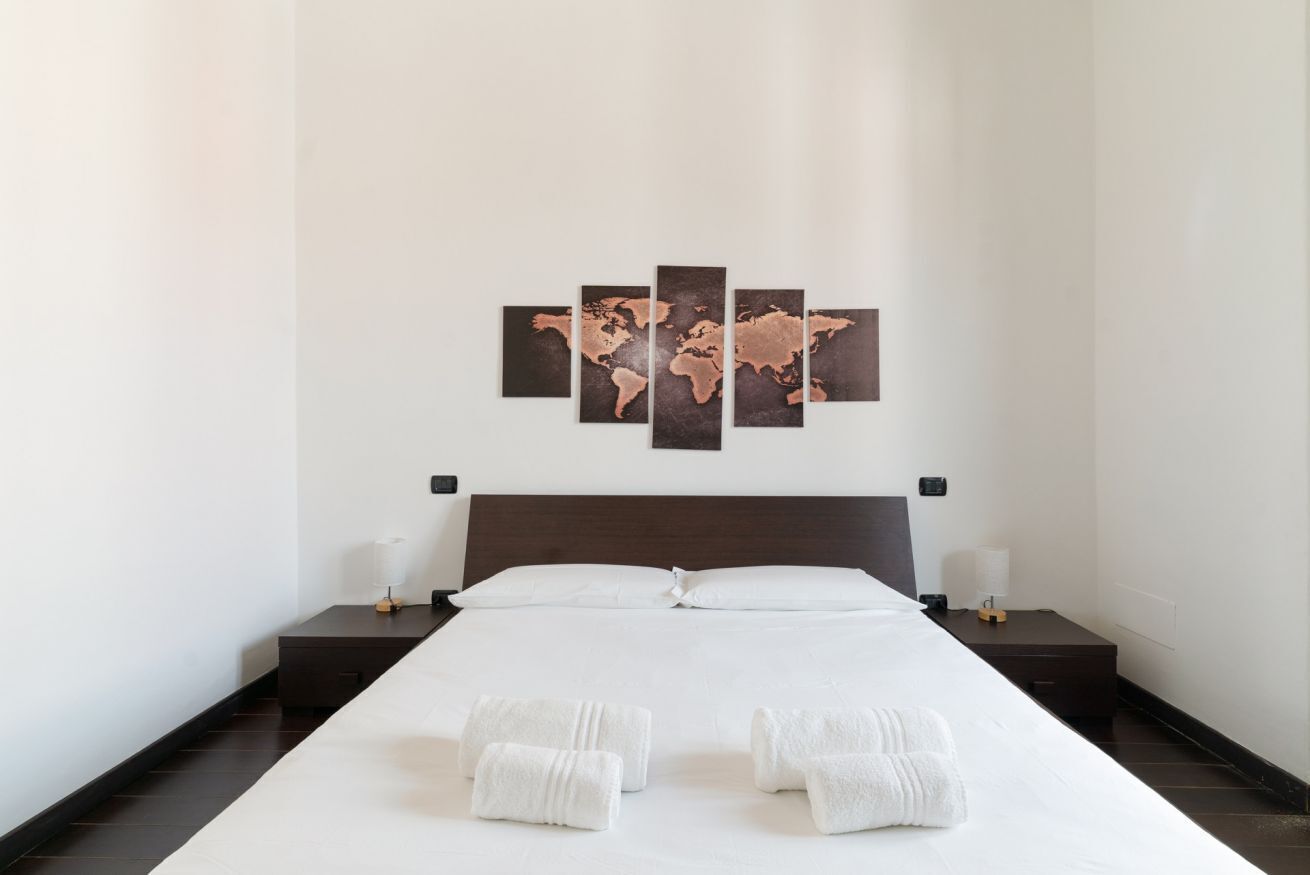Una camera d'albergo con un letto grande, un quadro raffigurante una mappa del mondo sulla parete e asciugamani ordinatamente piegati sul letto.
