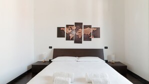 Habitación de hotel con una cama grande, un cuadro de un mapa mundial en la pared y toallas ordenadamente dobladas sobre la cama.