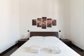 Habitación de hotel con una cama grande, un cuadro de un mapa mundial en la pared y toallas ordenadamente dobladas sobre la cama.