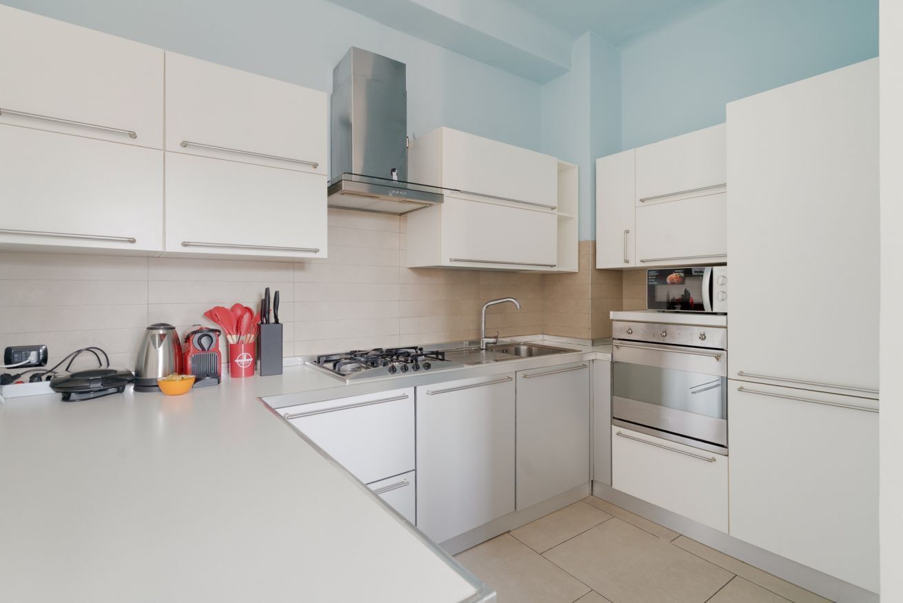 Una cucina moderna con mobili bianchi, piano cottura a gas, forno e cappa aspirante in acciaio inossidabile.