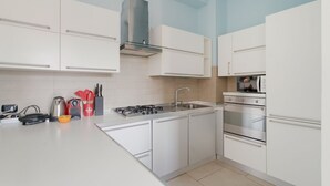Una cocina moderna con armarios blancos, estufa a gas, horno y campana extractora de acero inoxidable.