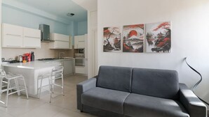 Una cocina moderna con armarios blancos, un sofá gris y tres cuadros en la pared.