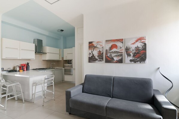 Eine moderne Küche mit weißen Schränken, einem grauen Sofa und drei Bildern an der Wand.