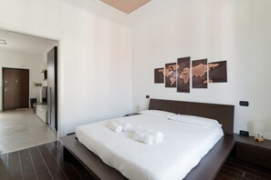 Ein modernes Hotelzimmer mit einem großen Bett, einem Flachbildfernseher, einem Nachttisch mit Lampe und einer Wandmalerei einer Weltkarte.