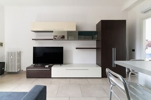 A modern living room with a flat-screen TV, built-in shelves, a dark cabinet, and a dining area with a table and chairs.