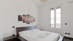Moderni hotellihuone, jossa on suuri sänky, yöpöytä, seinälle ripustettu taideteos ja ikkuna, josta on näkymä.