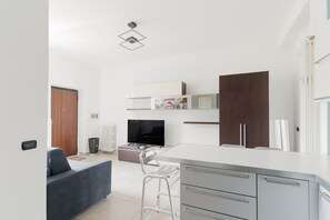 Una cocina moderna con armarios blancos, un mueble de madera oscura, un televisor y una zona de bar.