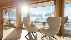 Ein modernes Interieur mit großen Fenstern, zwei weißen Stühlen und einer Holzbalkendecke.