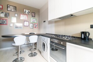 Una cucina moderna con lavatrice integrata, piano cottura a gas e un'area bar con sgabelli bianchi.