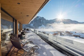 Un balcón con sillas, techo de madera y vistas a una montaña nevada y edificios.
