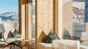 Een houten interieur met een groot raam, een comfortabele bank en een stoel met kussens.