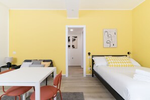 A room with a bed, a desk, a chair, and a door leading to another room.