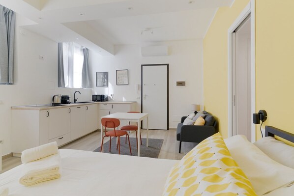 A compact hotel room with a bed, a small kitchenette, a dining area, and a sofa.